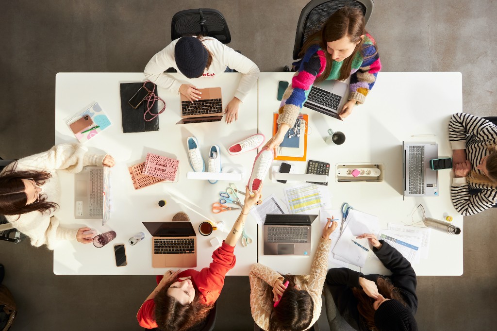 The EVG team working together at a table with products — sneakers, laptops and project materials seen from above