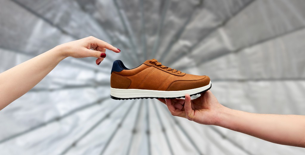 Two hands presenting a sneaker against a photographic umbrella backdrop — a packshot created at EVG Studio